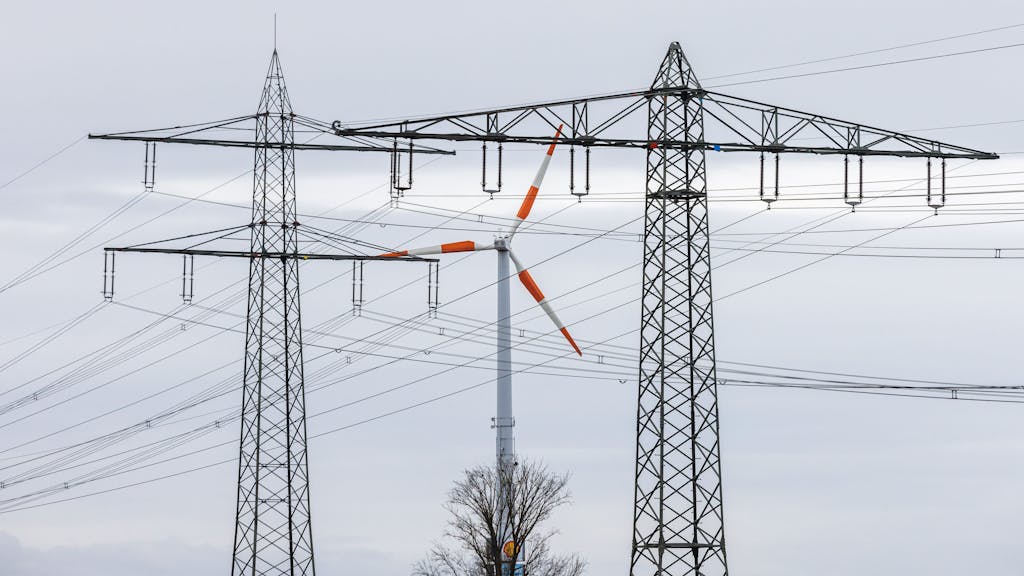 Ein Windrad steht neben dem Mast einer Hochspannungsleitung und dreht sich im Wind. Die Energieminister der EU-Länder haben am Freitag Notfallmaßnahmen gegen die gestiegenen Strompreise beschlossen.