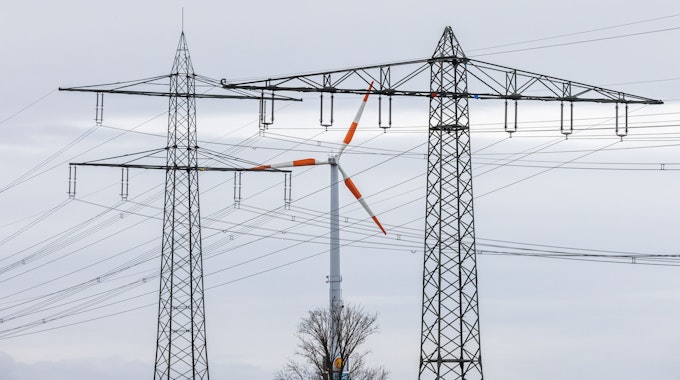 Ein Windrad steht neben dem Mast einer Hochspannungsleitung und dreht sich im Wind. Die Energieminister der EU-Länder haben am Freitag Notfallmaßnahmen gegen die gestiegenen Strompreise beschlossen.
