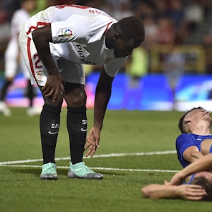 Joris Gnagnon, damals noch im Trikot des FC Sevilla, bückt sich, während zwei Gegenspieler verletzt auf dem Rasen liegen.