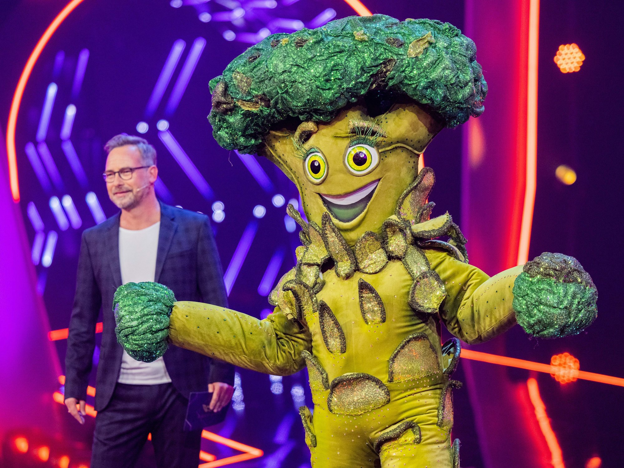 Die Figur „Der Brokkoli“ steht in der ProSieben-Show „The Masked Singer“ auf der Bühne neben Moderator Matthias Opdenhövel.