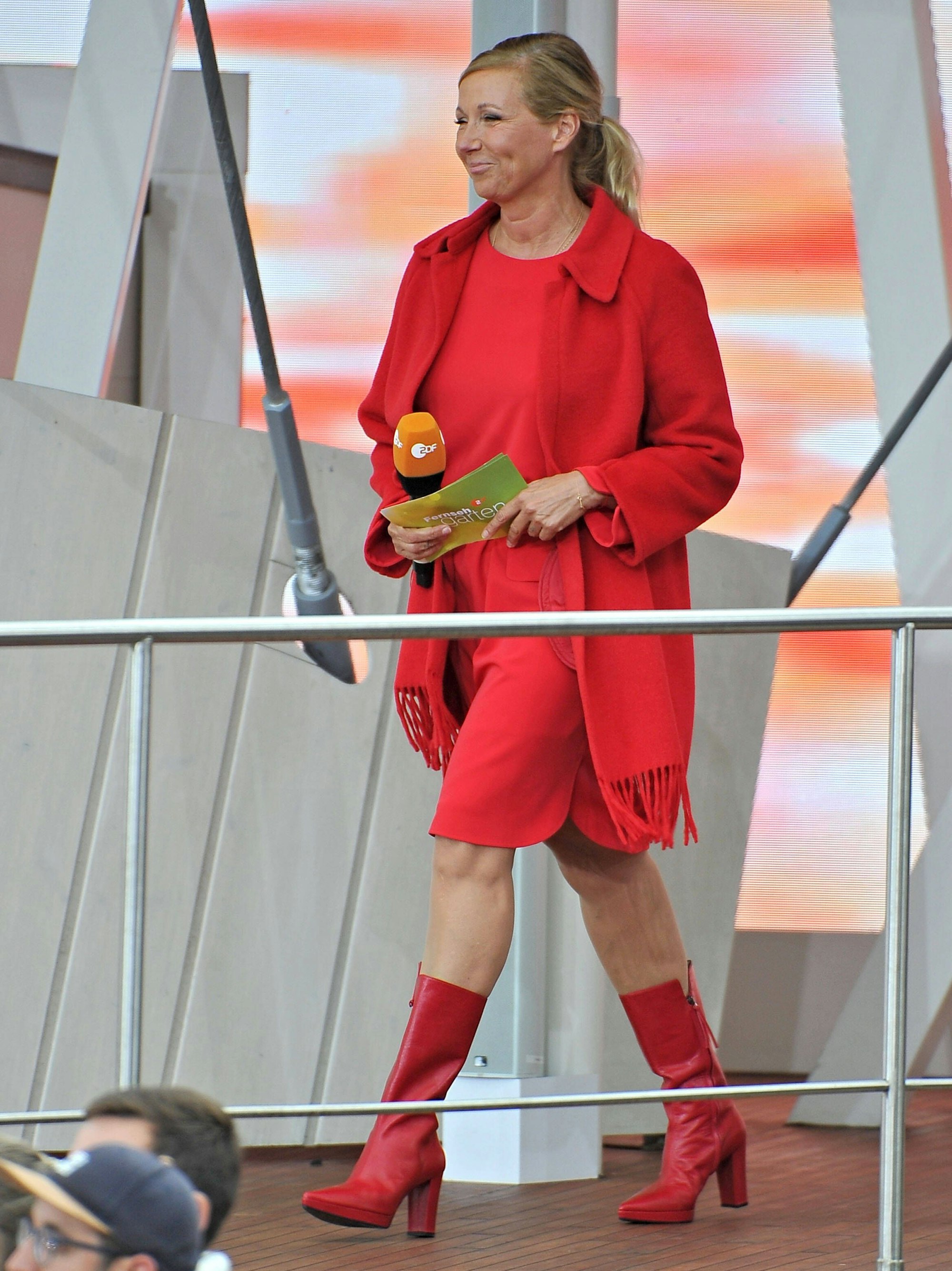 In roten Lederstiefeln und einem dazu farblich abgestimmten Kleid läuft „Fernsehgarten“-Moderatorin Andrea Kiewel auf die Bühne.