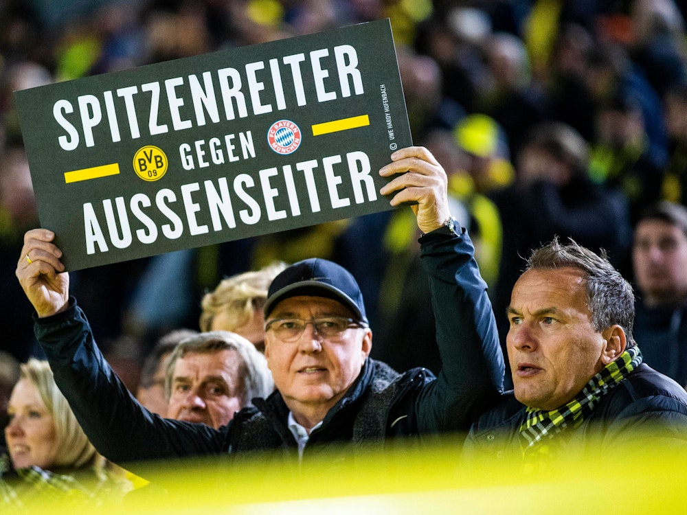 Ein Fan hält in Dortmund ein Plakat mit der Aufschrift Spitzenreiter gegen Außenseiter in die Luft.