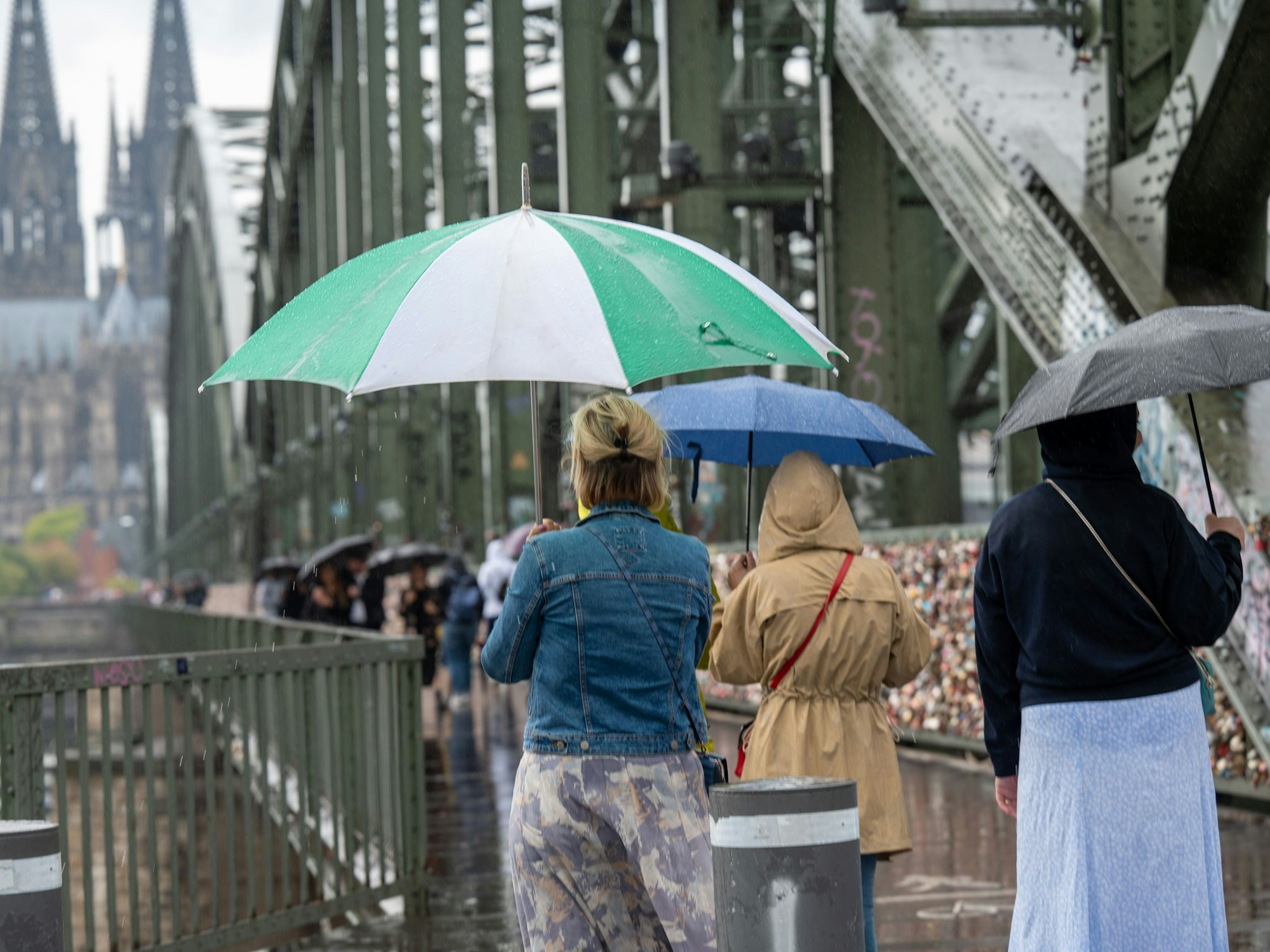 Menschen spazieren mit Regenschirmen über die Hohenzollernbrücke.