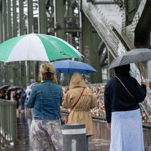 Menschen spazieren mit Regenschirmen über die Hohenzollernbrücke.