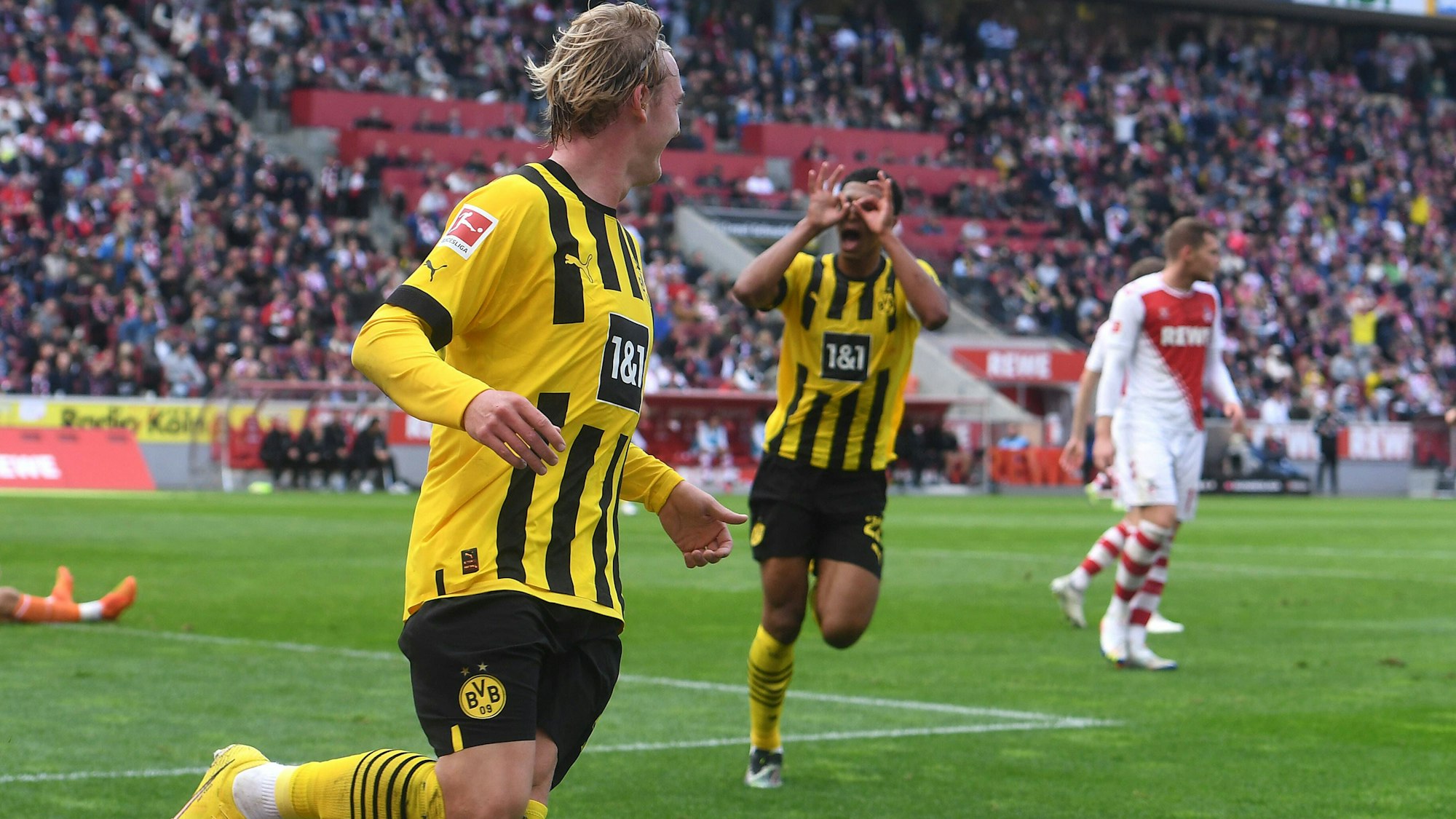 Julian Brandt (v.) feiert sein Tor zum 1:0 für Borussia Dortmund beim 1. FC Köln, Jude Bellingham zelebriert die Führung mit dem Modeste-Jubel.