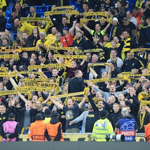 Fans von Borussia Dortmund halten auf der Tribüne ihre Fanschals hoch.