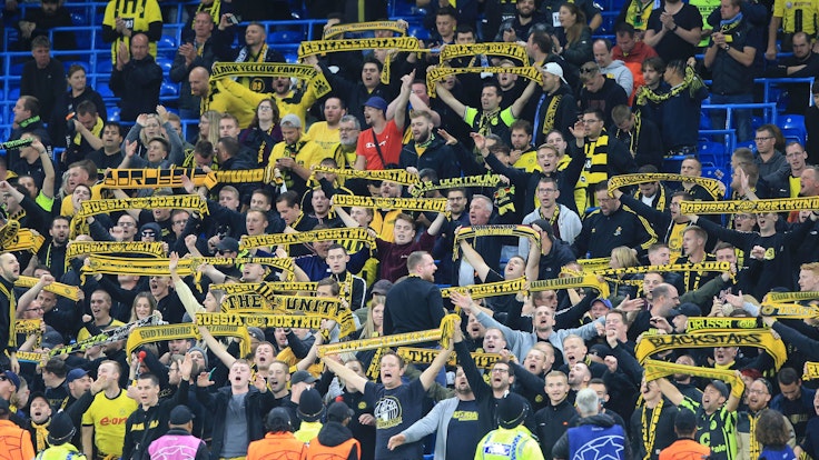 Fans von Borussia Dortmund halten auf der Tribüne ihre Fanschals hoch.