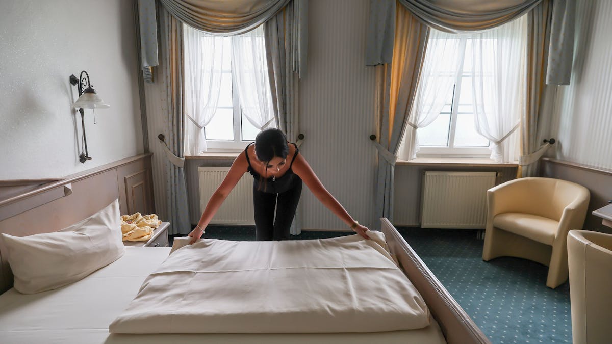 Eine Mitarbeiterin eines Hotels zieht eine Bettdecke in einem Hotelzimmer glatt.