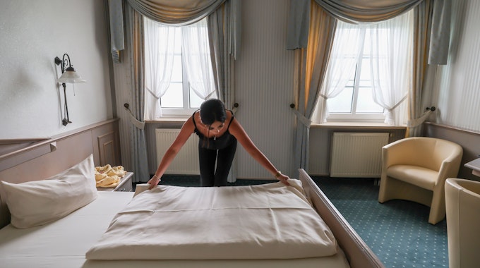 Eine Mitarbeiterin eines Hotels zieht eine Bettdecke in einem Hotelzimmer glatt.