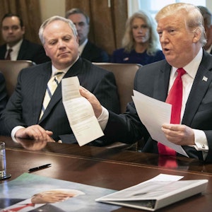 Donald Trump sitzt an einem Schreibtisch im Weißen Haus und zeigt ein Dokument.