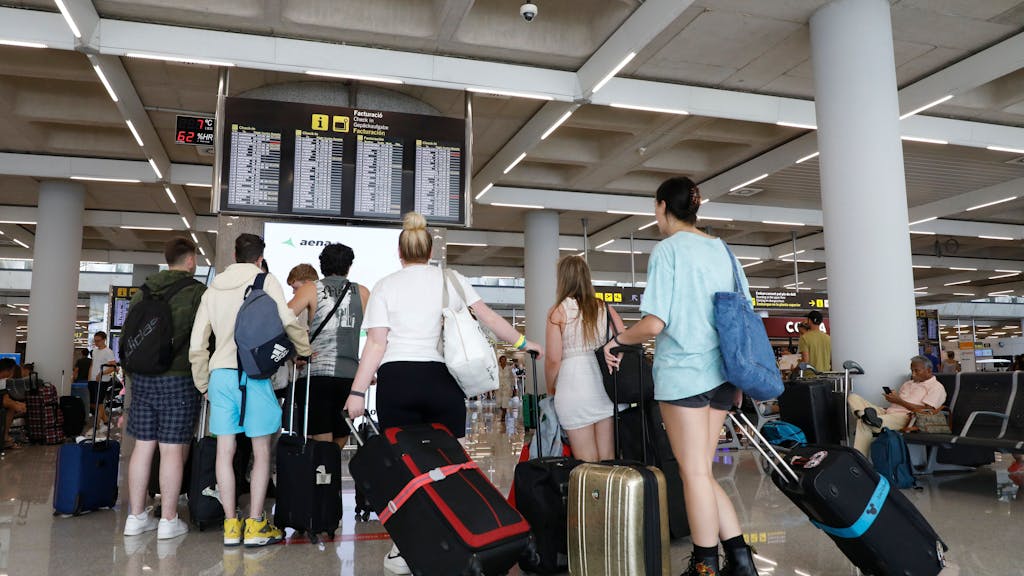 Reisende schauen am Flughafen auf die Anzeigetafel mit den Flugzeiten.