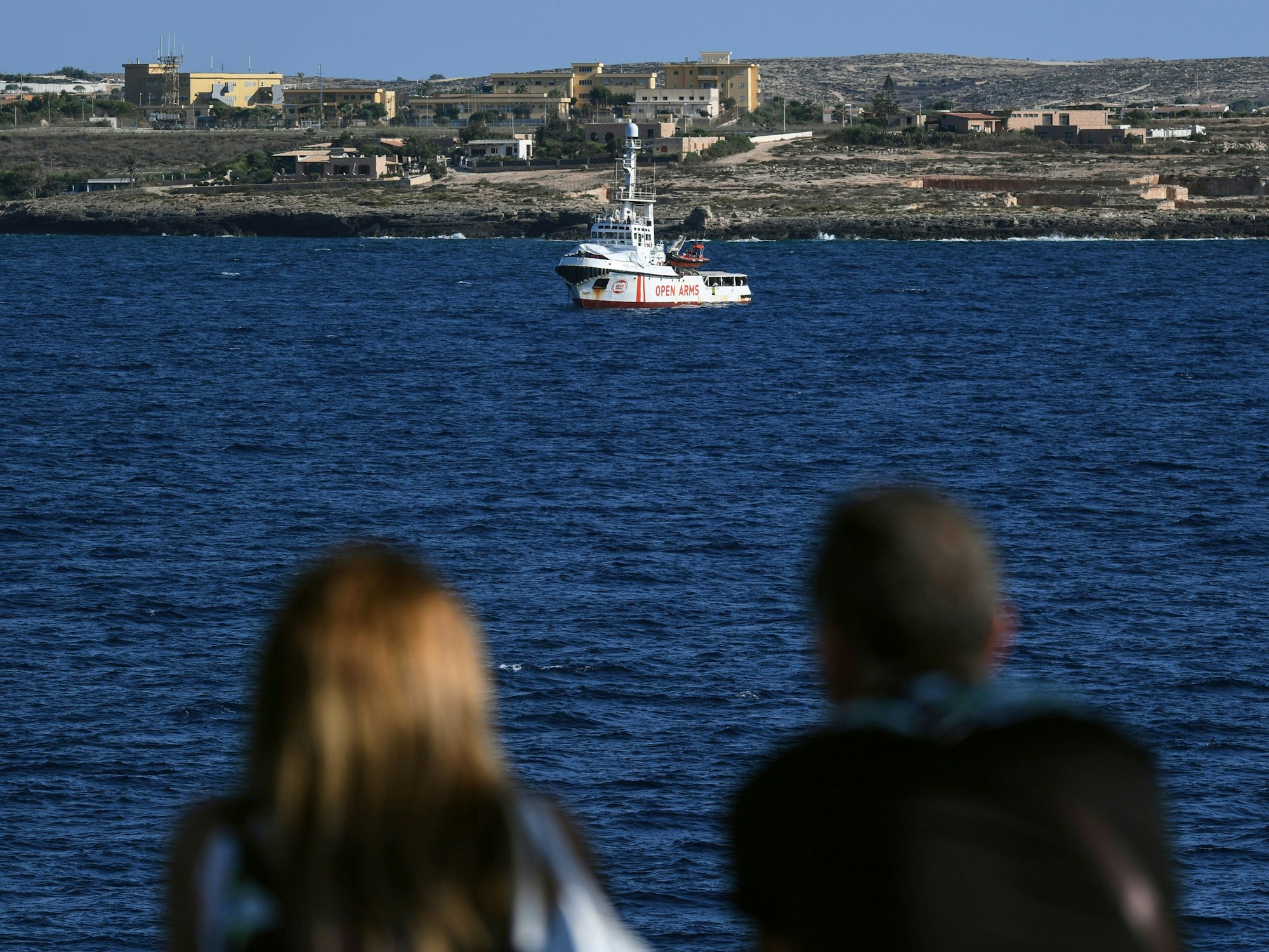 Zwei Menschen auf einer Fähre schauen auf das Rettungsschiff „Open Arms“ der Hilfsorganisation Proactiva. Die Aufnahme dient hier als Symbolfoto.