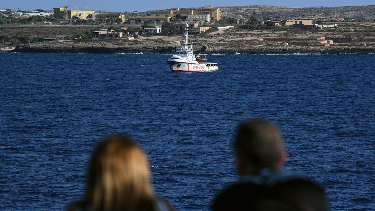 Zwei Menschen auf einer Fähre schauen auf das Rettungsschiff „Open Arms“ der Hilfsorganisation Proactiva. Die Aufnahme dient hier als Symbolfoto.