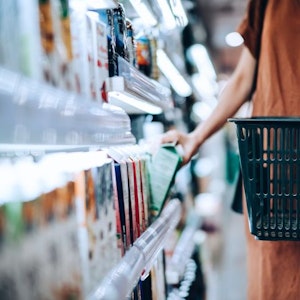 Auf dem Bild ist eine Person zu sehen, die im Supermarkt mit einem Einkaufskorb nach einer Milch greift.