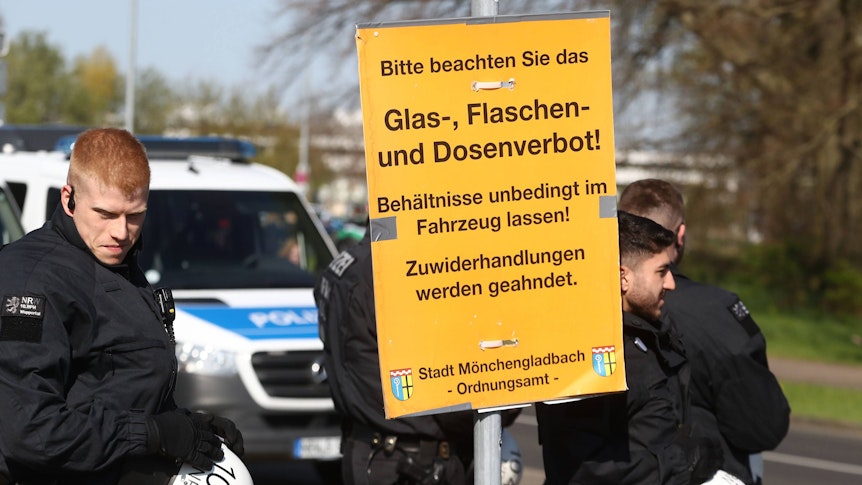 Wie in jedem Jahr wird es rund um das Derby zwischen Borussia Mönchengladbach und dem 1. FC Köln zahlreiche Sicherheitsmaßnahmen geben. Das Foto zeigt Polizeibeamte beim vergangenen Derby am 16. April 2022 mit einem Schild, dass auf das Glas-, Flaschen- und Dosenverbot hinweist.
