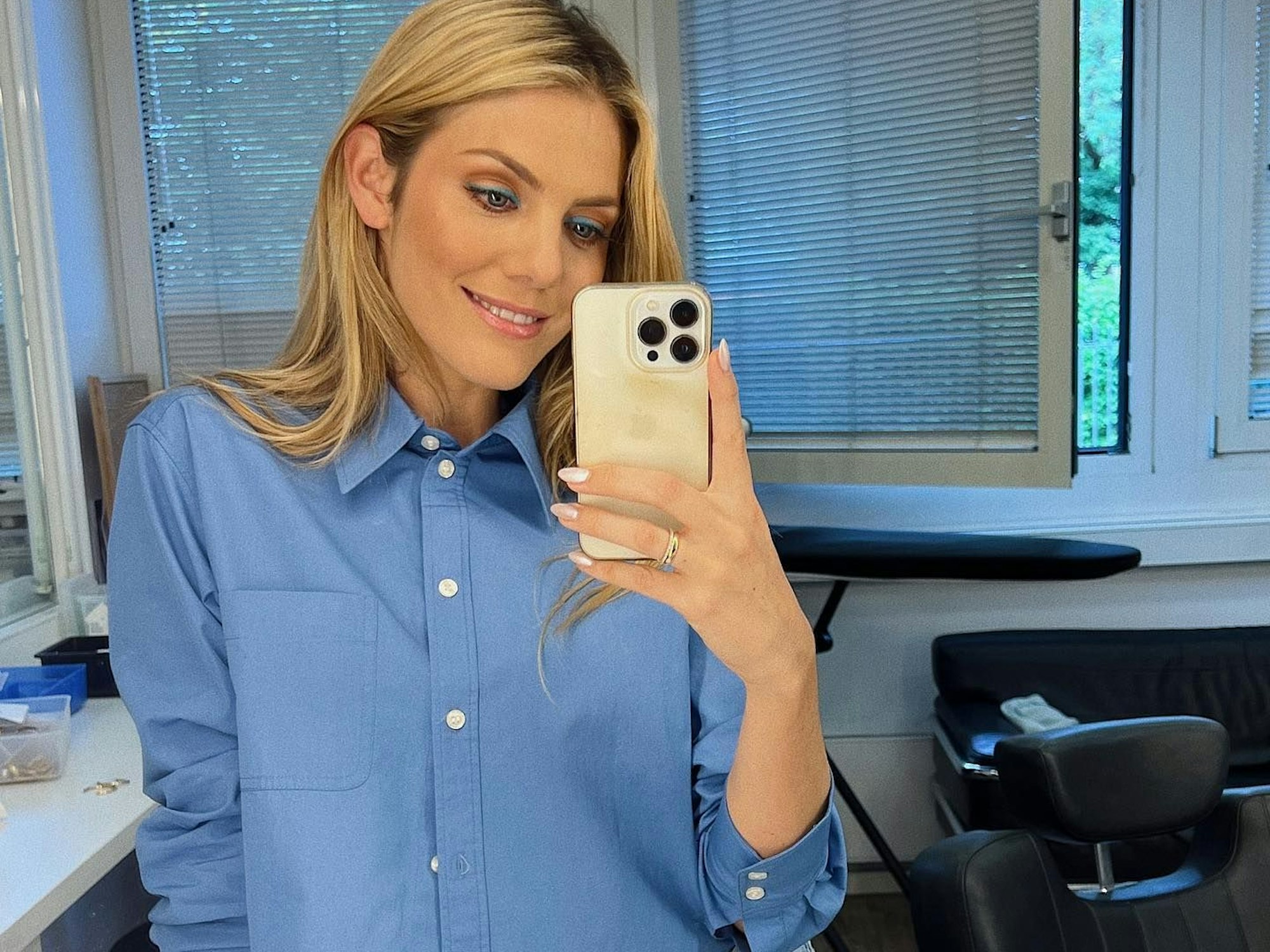 Viviane posiert für ein Spiegel-Selfie in einer blauen Bluse.
