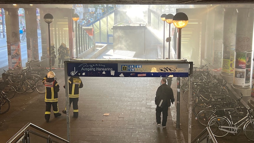 Mehrere Feuerwehrleute gehen auf eine Treppe zur U-Bahn zu, aus der Rauch dringt.