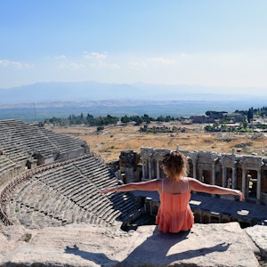 Eine Touristin breitet die Arme aus während sie auf den Ruinen der antiken Stadt und UNESCO-Weltkulturerbe Hierapolis sitzt.