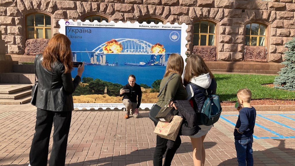 Menschen fotografieren sich am 9. Oktober 2022 in Kyjiw vor einem Plakat, das Explosionen auf der für Russland wichtigen Krym-Brücke zeigt.