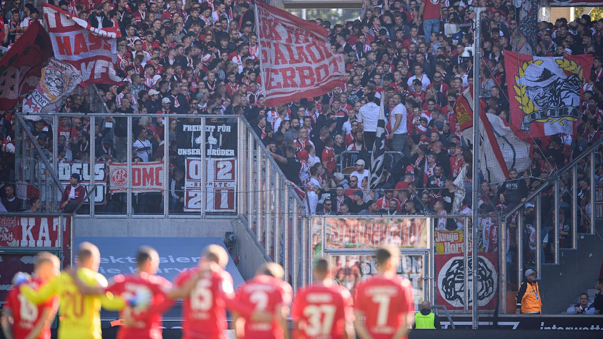 Die FC-Spieler umarmen sich bei einer Schweigeminute, Kölner Fans schwenken Fahnen.