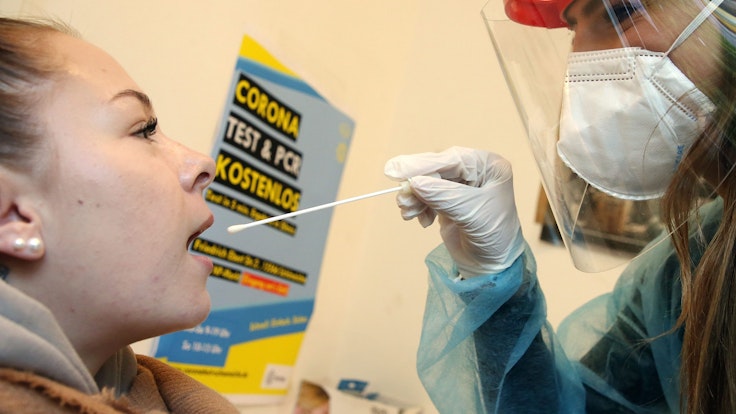 Eine junge Frau lässt von einer Mitarbeiterin einer Corona-Teststelle mit einem Teststäbchen einen Abstrich machen, um sich auf Corona zu testen.