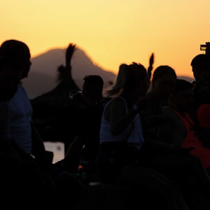 Das undatierte Symbolfoto zeigt mehrere Menschen, die vor einem Sonnenuntergang feiern.