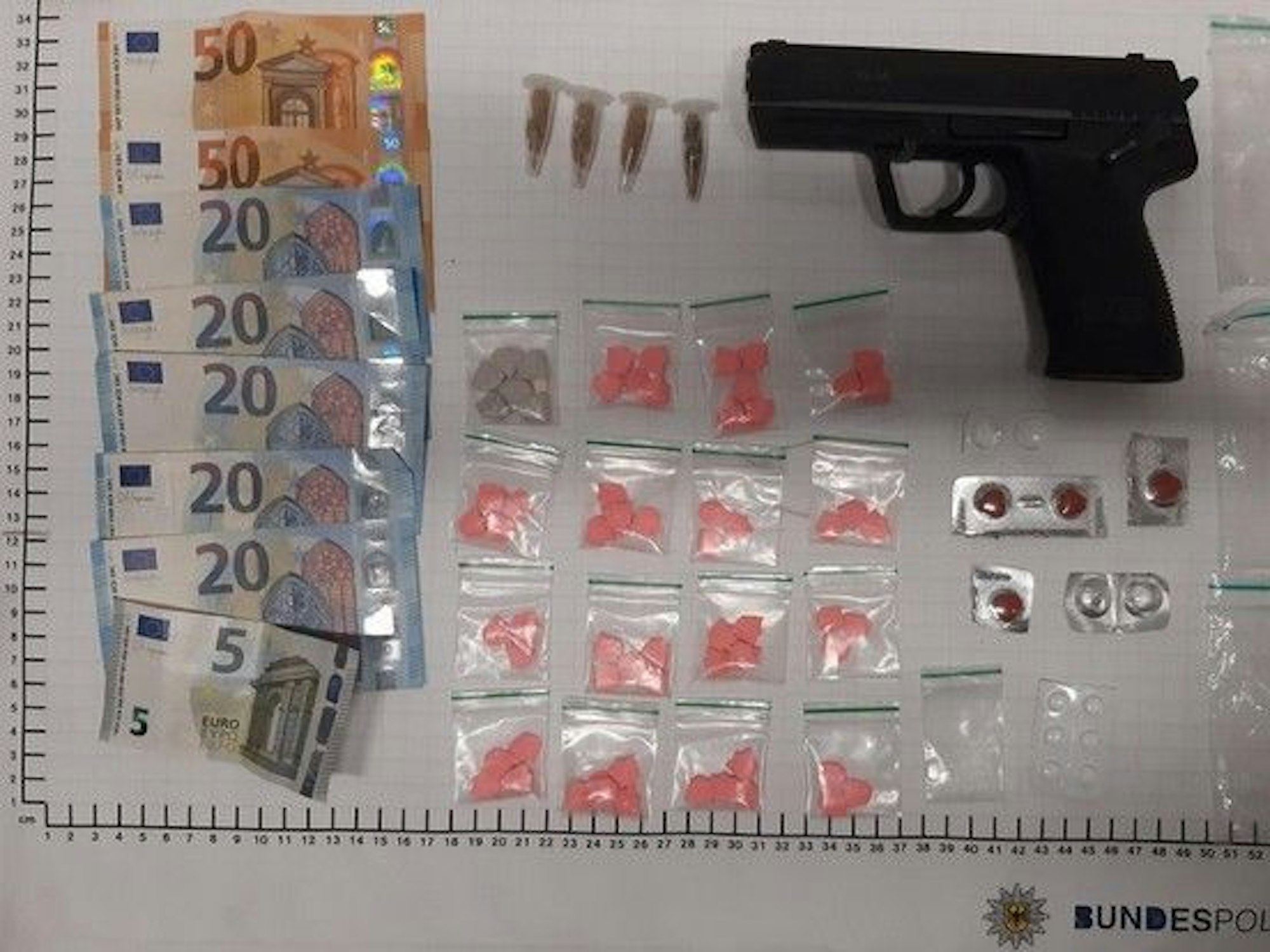 Bargeld, Tüten mit Drogen und eine Pistole liegen auf einem weißen Tisch.