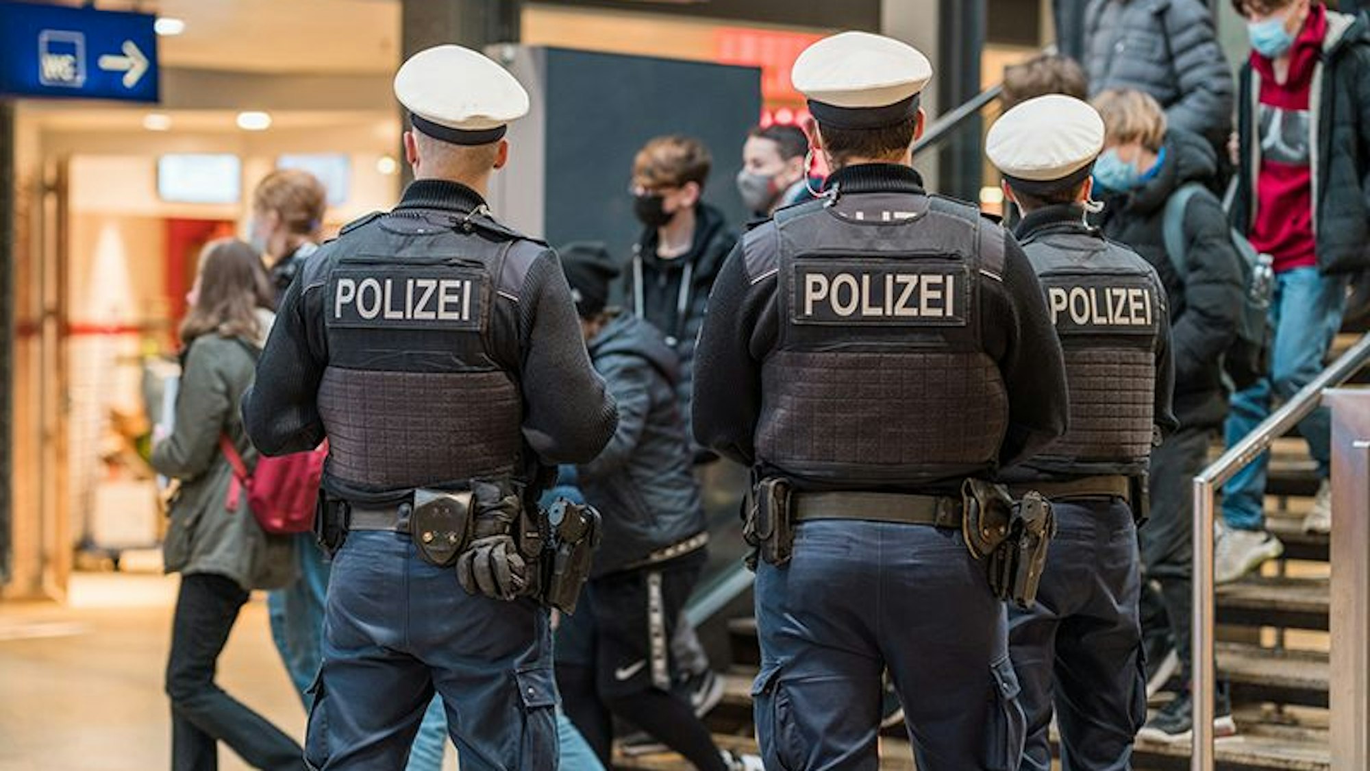 Drei Bundespolizisten stehen im Kölner Hauptbahnhof und beobachten Reisende, die eine Treppe herunterkommen.