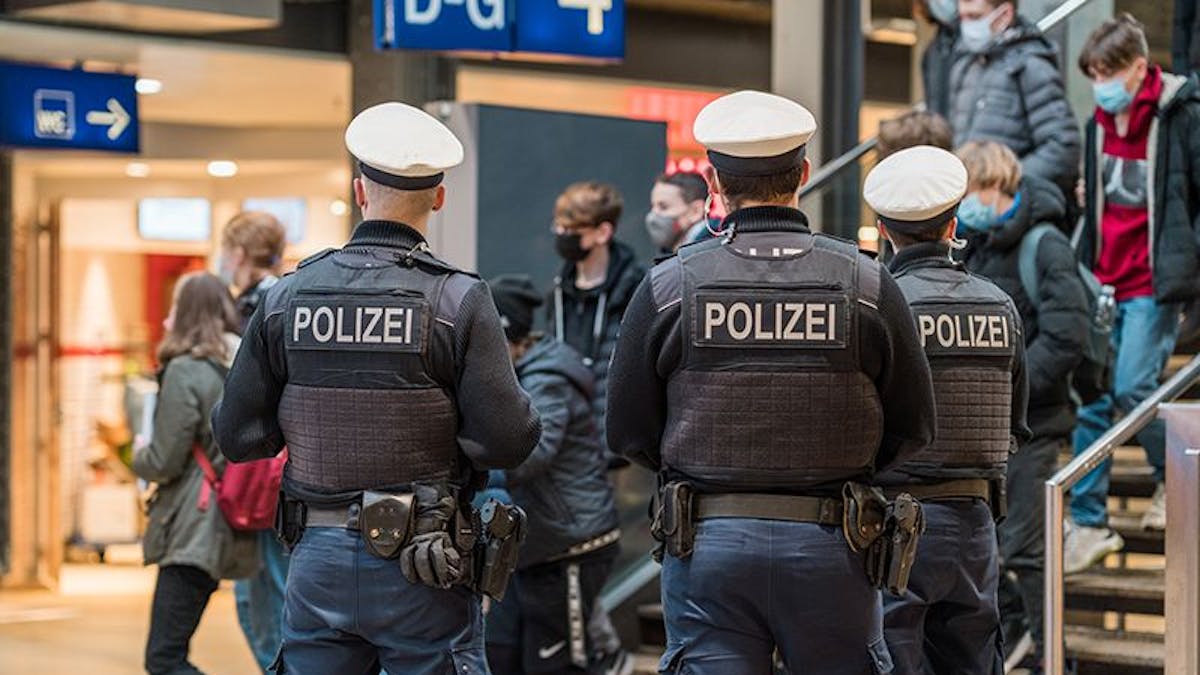 Drei Bundespolizisten stehen im Kölner Hauptbahnhof und beobachten Reisende, die eine Treppe herunterkommen.
