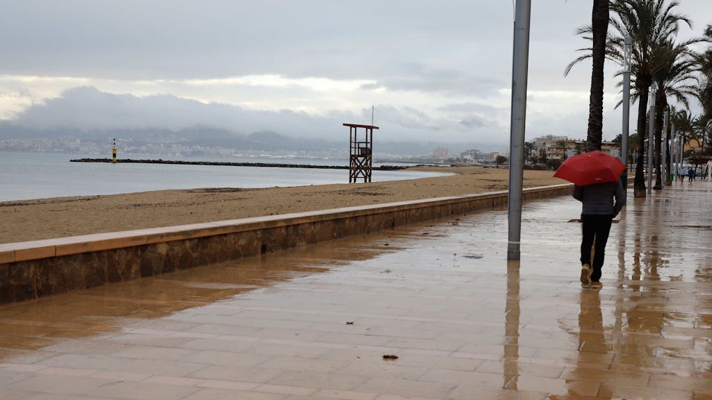 Ein Mann spaziert mit einem Regenschirm am Strand von Palma entlang.&nbsp;
