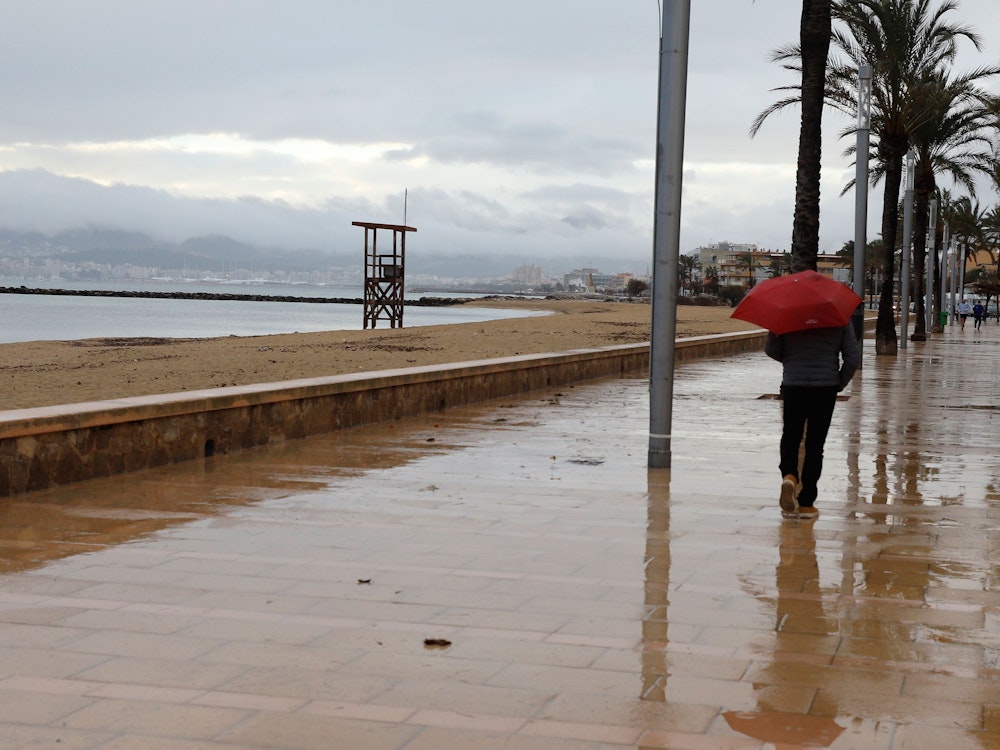 Ein Mann spaziert mit einem Regenschirm am Strand von Palma entlang.