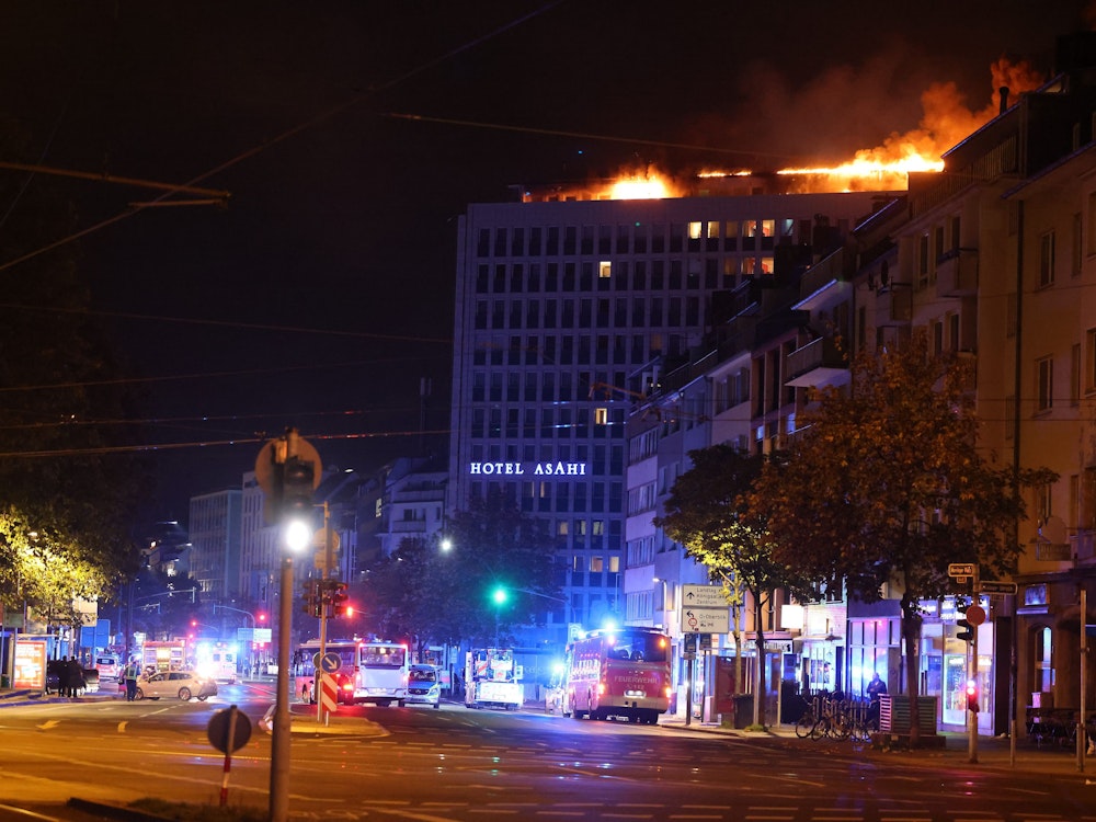 Flammen schlagen aus dem Dach eines Hotels in der Düsseldorfer Innenstadt während die Feuerwehr im Einsatz ist.