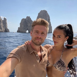 Jörn und Hanna posieren für ein Selfie auf einem Boot. Sie trägt einen Bikini, er ein braunes Poloshirt.