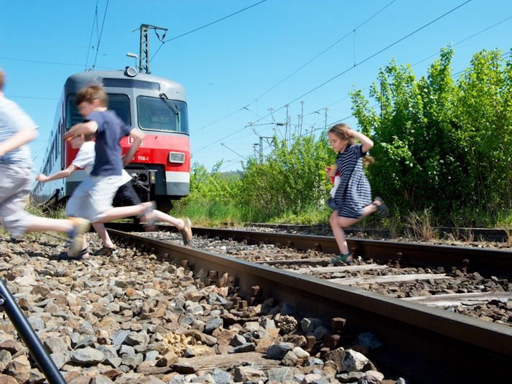 Auf einem Symbolfoto sind spielende Kinder zu sehen, die vor einer Bahn über die Gleise laufen.