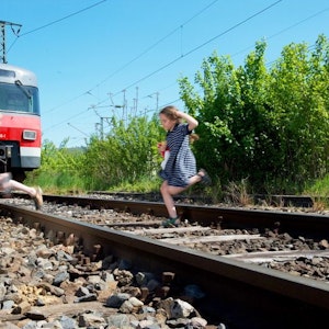 Auf einem Symbolfoto sind spielende Kinder zu sehen, die vor einer Bahn über die Gleise laufen.