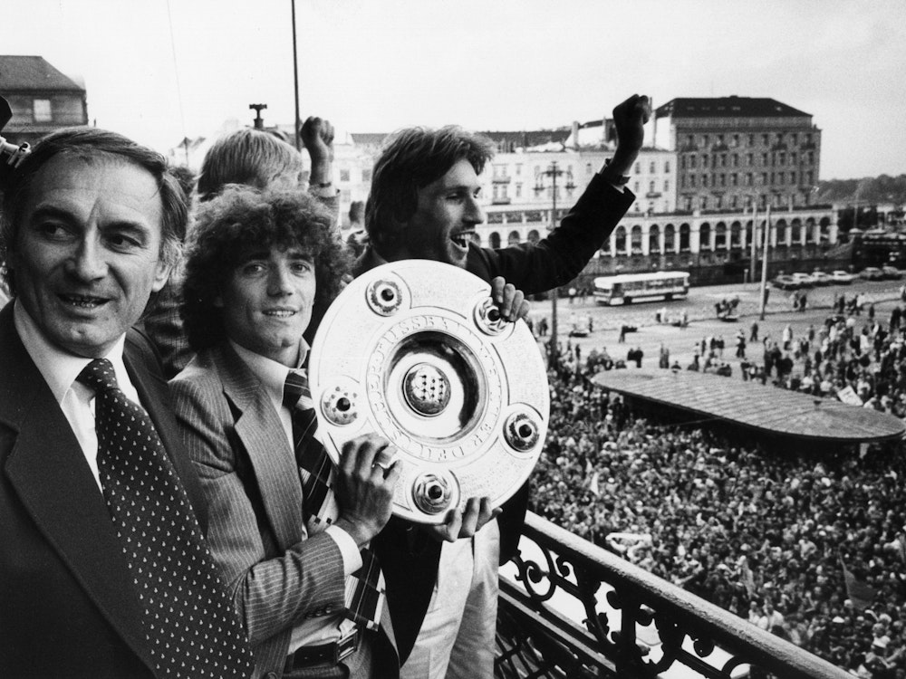 Neben dem jugoslawische Trainer Branco Zebec (l) und Abwehrspieler Manfred Kaltz (r) zeigt der englische Stürmerstar Kevin Keegan (M) vom Hamburger SV die Meisterschale am 9. Juni 1979.