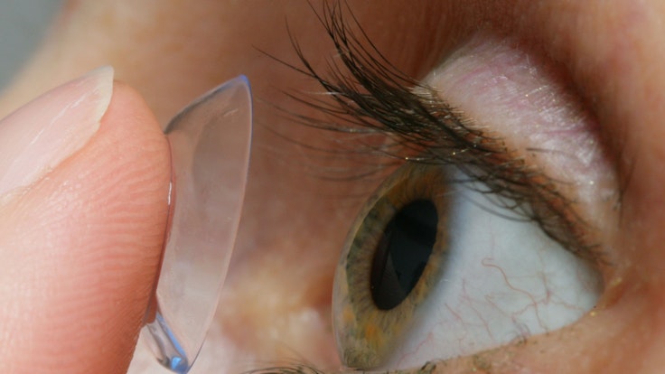 Eine Frau setzt sich eine Kontaktlinse auf das Auge.