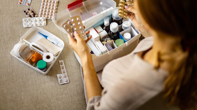 Person hat Tabletten in der Hand. Box mit Medikamenten und Verbandszeug. Bild für Amazon-Artikel.