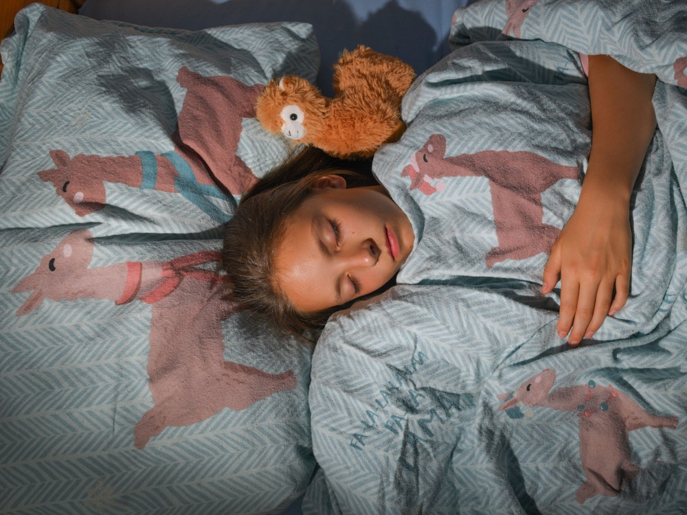 Ein Mädchen schläft in ihrem Bett mit Lama-Bettwäsche (gestellte Szene).