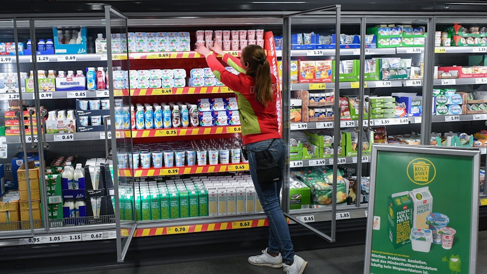Ein Mitarbeitern ordnet die Milchprodukte in einem Kühlregal im Lebensmittel-Discounter Penny, vor dem der Aufsteller mit der Werbung der Kampagne «Kostbares retten» steht.