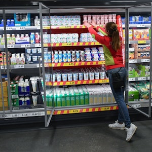Ein Mitarbeitern ordnet die Milchprodukte in einem Kühlregal im Lebensmittel-Discounter Penny, vor dem der Aufsteller mit der Werbung der Kampagne «Kostbares retten» steht.