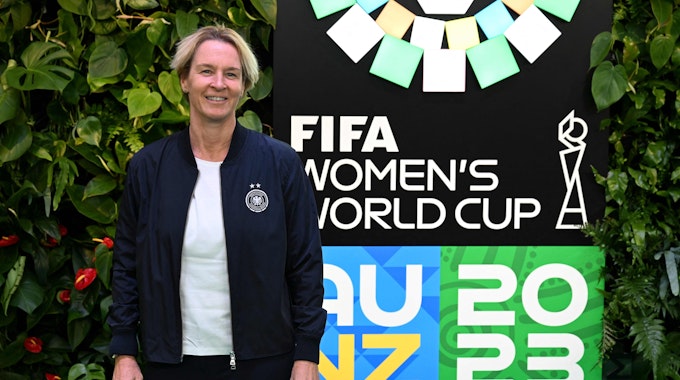 Martina Voss-Tecklenburg steht vor dem Logo der WM 2023.