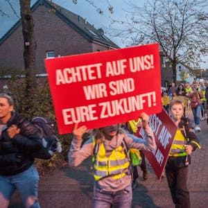 Kinder mit Plakaten und in elterlicher Begleitung protestieren in der Dämmerung auf der Hitdorfer Ringstraße für mehr Sicherheit