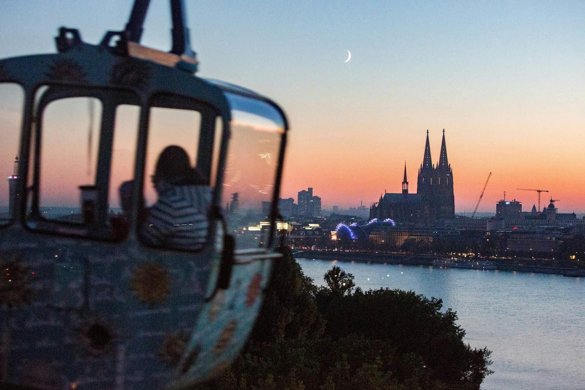 Eine Gondel der Rheinseilbahn vor dem abendlichen Köln-Panorama mit Dom