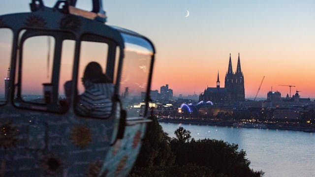 Eine Gondel der Seilbahn vor dem Köln-Panorama in der Dämmerung