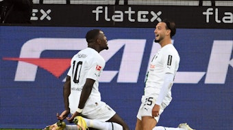 Die Gladbach-Stars Marcus Thuram (l.) und Ramy Bensebaini (r.) jubeln gemeinsam über einen Treffer im Borussia-Park, hier zu sehen am 17. September 2022 beim Bundesliga-Duell gegen RB Leipzig. Die beiden knien auf dem Rasen.