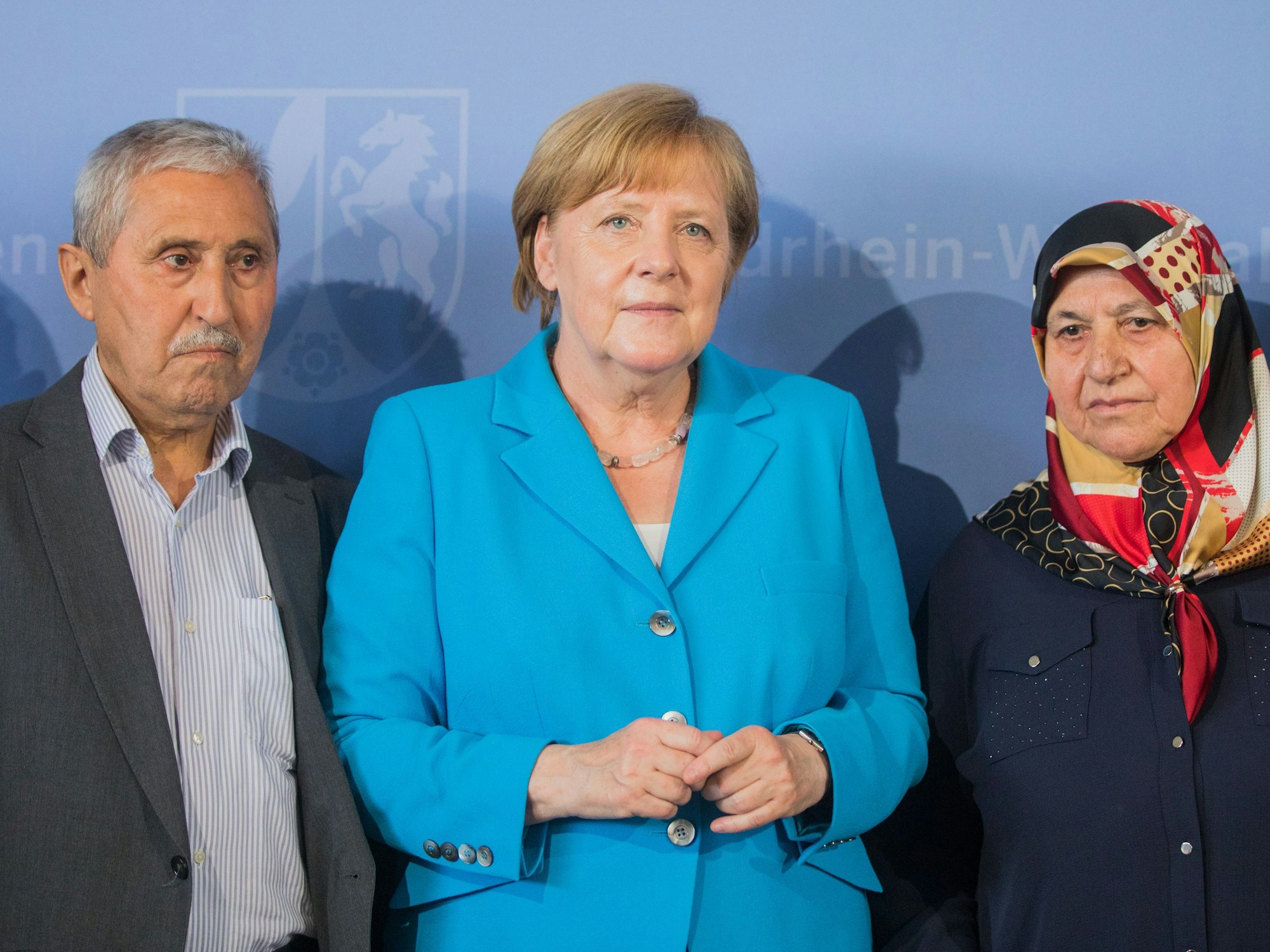 Kanzlerin Merkel steht mit Mevlüde und Durmus Genc auf einem Podium.