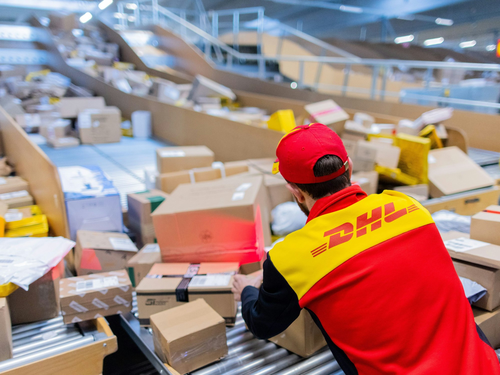 Ein Paketzusteller sortiert und räumt in einer Zustellbasis von Deutsche Post DHL Pakete in ein Zustellfahrzeug.