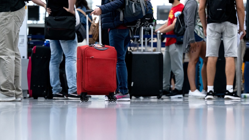Passagiere stehen mit ihrem Gepäck an einem Check-in-Schalter am Flughafen München.