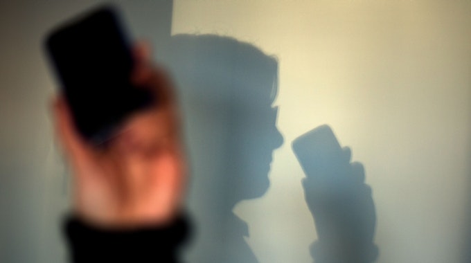 Eine Frau telefoniert mit ihrem Mobiltelefon und wirft dabei einen Schatten auf eine Wand.
